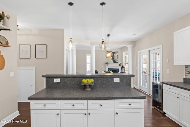 kitchen with beverage cooler, a fireplace, dark countertops, dark wood finished floors, and decorative columns