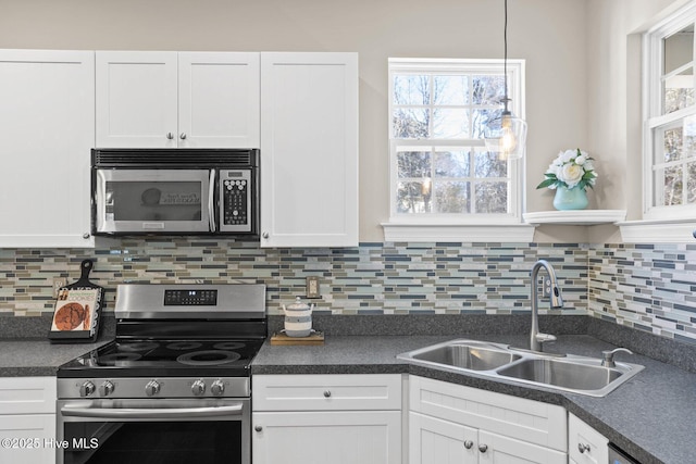 kitchen featuring decorative backsplash, dark countertops, stainless steel appliances, white cabinetry, and a sink