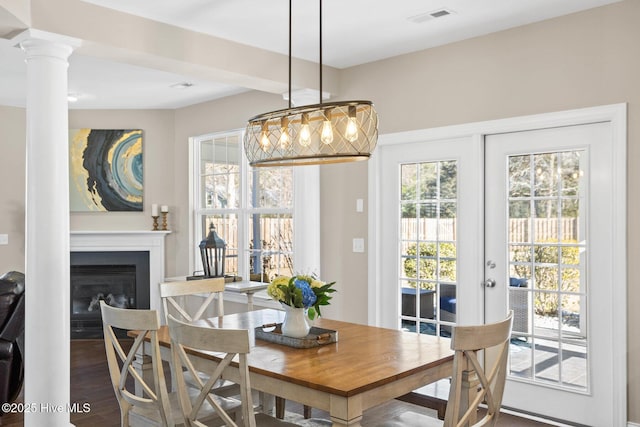 dining room featuring french doors, decorative columns, visible vents, a glass covered fireplace, and wood finished floors