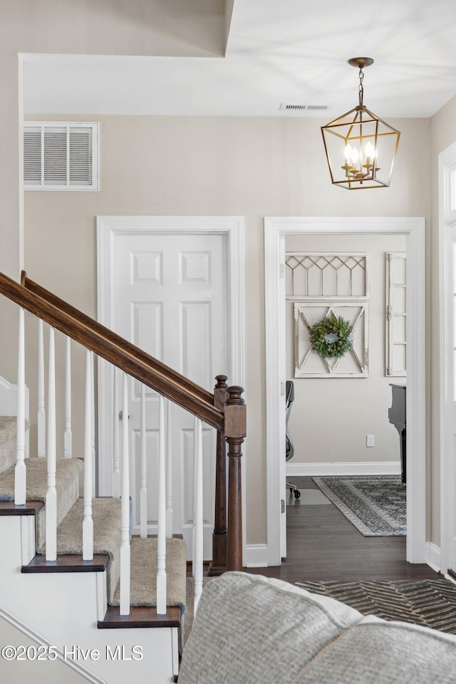 foyer entrance with a chandelier, stairway, wood finished floors, and visible vents