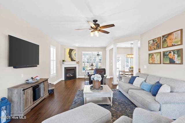 living room featuring ceiling fan, dark wood-style flooring, a fireplace with flush hearth, baseboards, and decorative columns