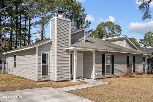 view of front of property featuring a shingled roof, a chimney, and a front lawn