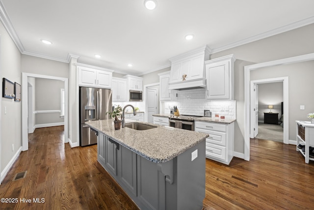 kitchen with a sink, visible vents, appliances with stainless steel finishes, a center island with sink, and custom range hood