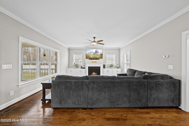 living area featuring dark wood finished floors, visible vents, ornamental molding, a warm lit fireplace, and baseboards