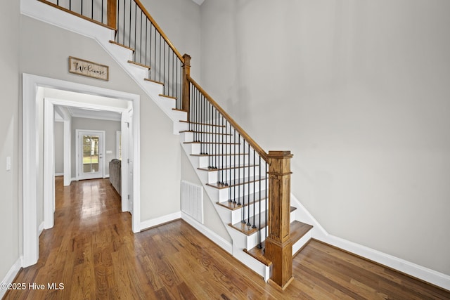 staircase featuring a high ceiling, visible vents, baseboards, and wood finished floors