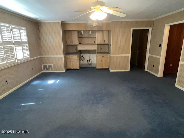 unfurnished living room featuring dark colored carpet, visible vents, ornamental molding, a ceiling fan, and wallpapered walls