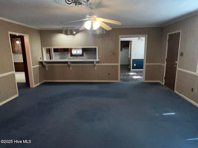 unfurnished living room with ornamental molding, dark colored carpet, and ceiling fan