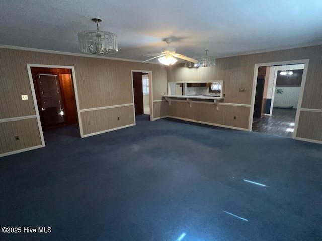 unfurnished living room featuring dark carpet, crown molding, and ceiling fan with notable chandelier