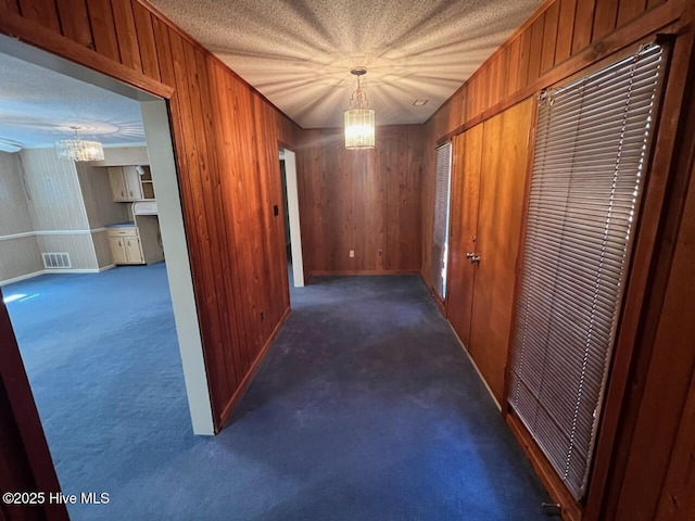 corridor with visible vents, a textured ceiling, carpet flooring, wood walls, and a notable chandelier