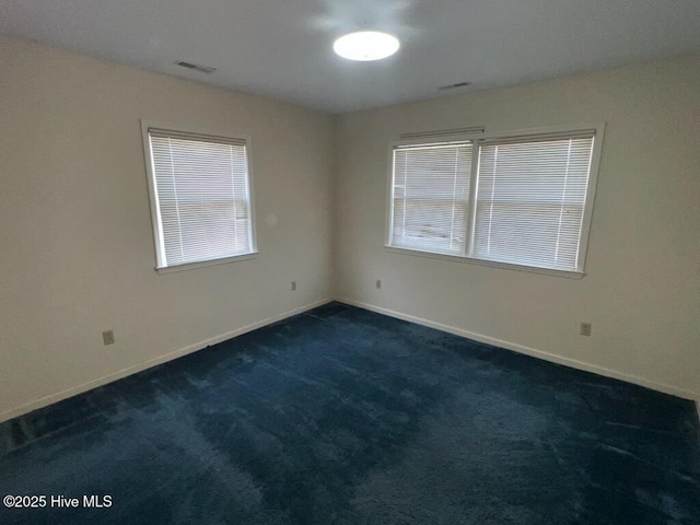 spare room with plenty of natural light, visible vents, dark carpet, and baseboards