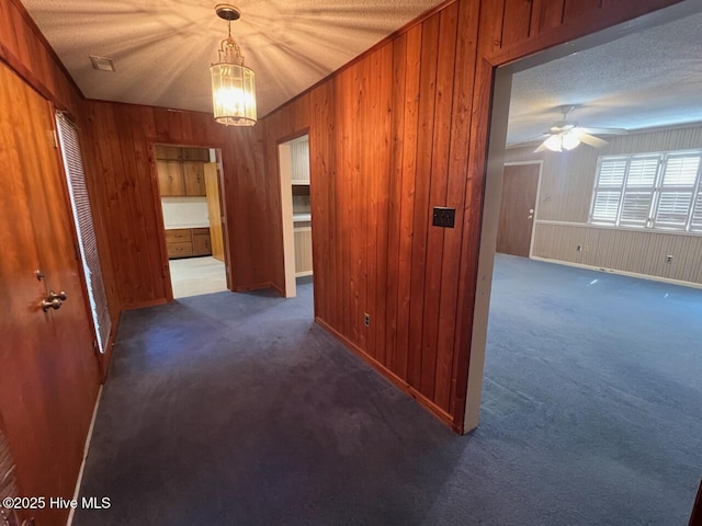 corridor featuring a textured ceiling, wooden walls, baseboards, and carpet flooring