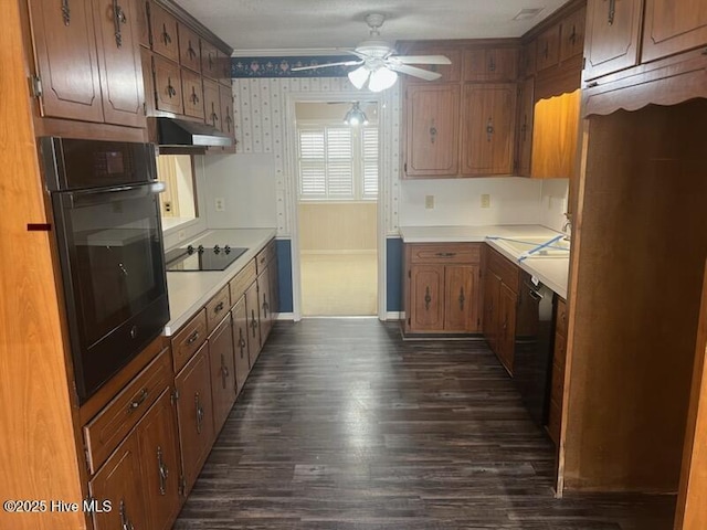 kitchen featuring black appliances, under cabinet range hood, light countertops, and wallpapered walls