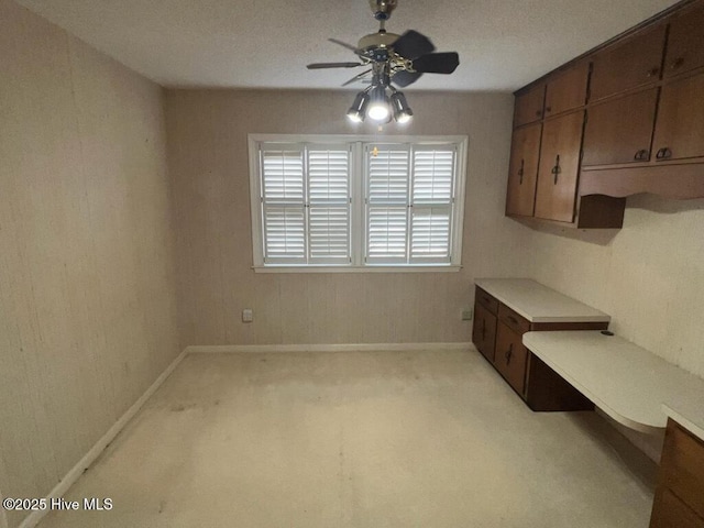 unfurnished dining area with light carpet, baseboards, and a ceiling fan