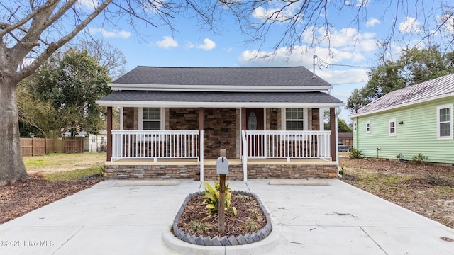 view of front of house featuring stone siding, a porch, a shingled roof, and fence