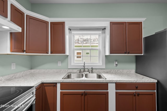 kitchen with light countertops, under cabinet range hood, freestanding refrigerator, and a sink