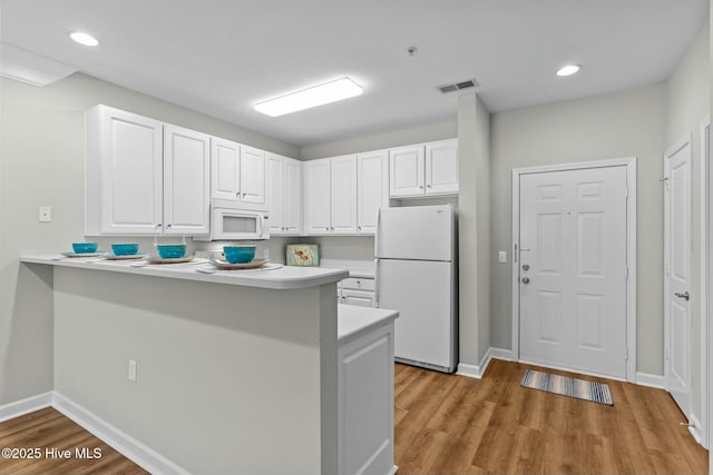 kitchen featuring a peninsula, white appliances, visible vents, white cabinetry, and light countertops