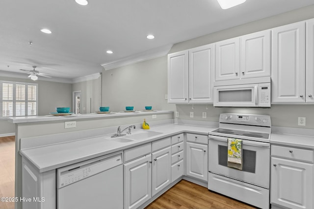 kitchen with a peninsula, white appliances, a sink, white cabinetry, and light wood finished floors