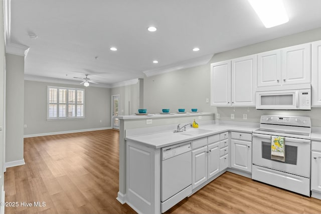 kitchen featuring a peninsula, white appliances, a sink, white cabinets, and ornamental molding