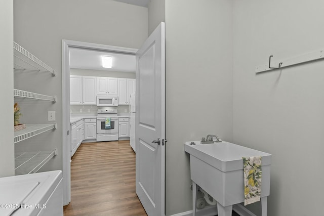 kitchen featuring light countertops, white cabinetry, a sink, wood finished floors, and white appliances