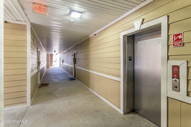 corridor featuring elevator, concrete flooring, and wood walls