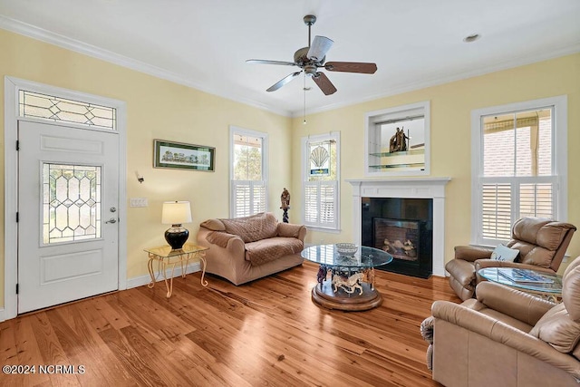 living area with a wealth of natural light, ornamental molding, wood finished floors, and a glass covered fireplace