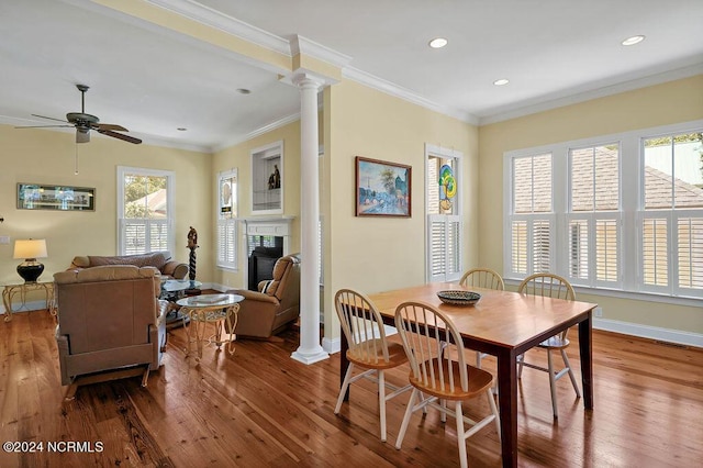 dining room featuring ornamental molding, a glass covered fireplace, ornate columns, and wood finished floors