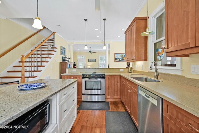 kitchen with pendant lighting, appliances with stainless steel finishes, ornamental molding, a sink, and wood finished floors