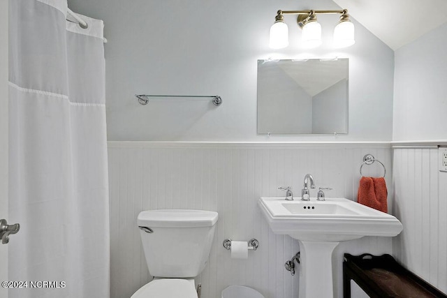 full bath featuring toilet, a wainscoted wall, a shower with shower curtain, and lofted ceiling