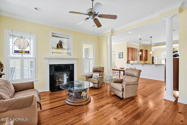 living area with ornate columns, light wood-style flooring, ornamental molding, and a glass covered fireplace