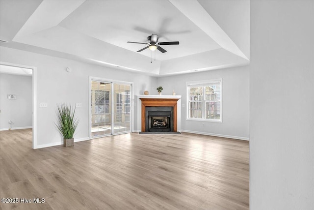 unfurnished living room featuring baseboards, a raised ceiling, a ceiling fan, light wood-style floors, and a fireplace