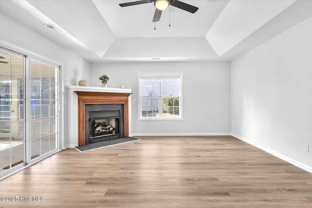 unfurnished living room with light wood finished floors, a fireplace, visible vents, and a tray ceiling