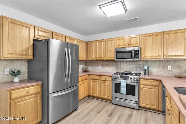 kitchen with light countertops, appliances with stainless steel finishes, decorative backsplash, and light wood-style floors