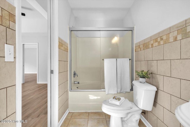 bathroom featuring enclosed tub / shower combo, toilet, tile patterned flooring, and tile walls