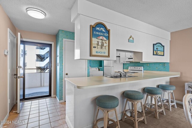 kitchen with a textured ceiling, white appliances, a sink, a kitchen breakfast bar, and washer / dryer