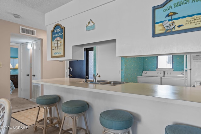 kitchen featuring a textured ceiling, a sink, visible vents, independent washer and dryer, and a kitchen bar