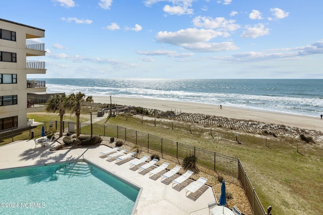 community pool featuring a view of the beach, a patio area, a water view, and fence