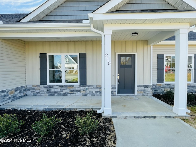 entrance to property featuring stone siding, a porch, and roof with shingles