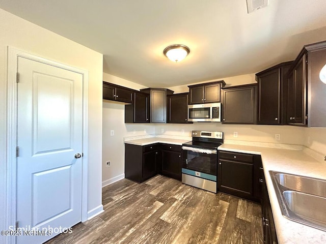 kitchen featuring visible vents, appliances with stainless steel finishes, dark wood-type flooring, a sink, and dark brown cabinets