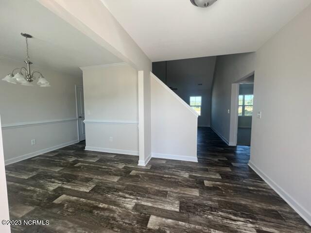 empty room with a notable chandelier, dark wood finished floors, and baseboards