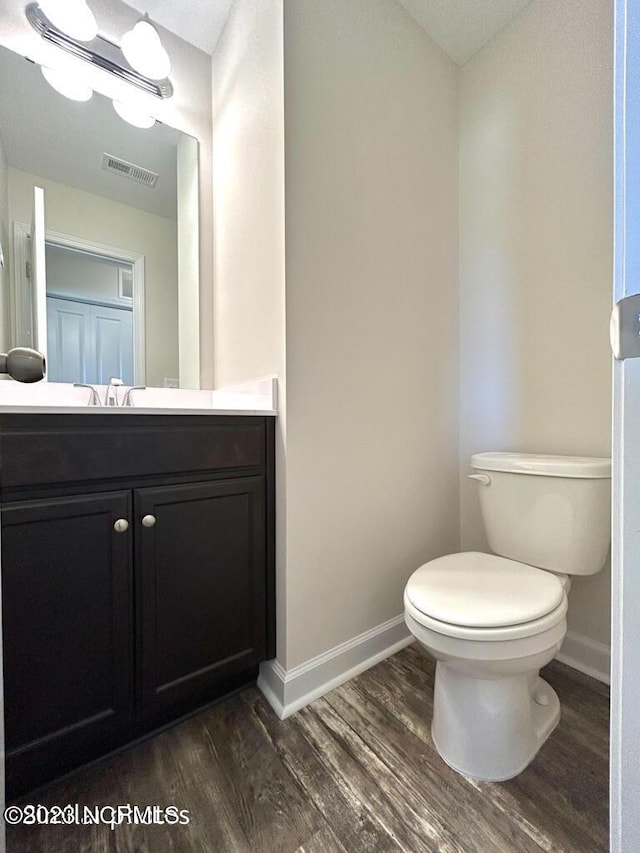 half bath featuring toilet, wood finished floors, vanity, visible vents, and baseboards