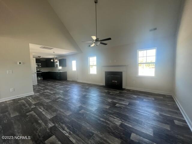 unfurnished living room featuring a fireplace, dark wood finished floors, visible vents, and baseboards