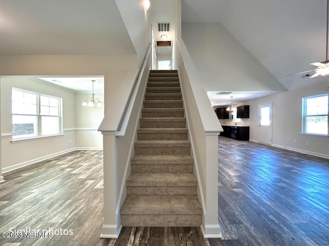 stairs featuring visible vents, baseboards, wood finished floors, and ceiling fan with notable chandelier