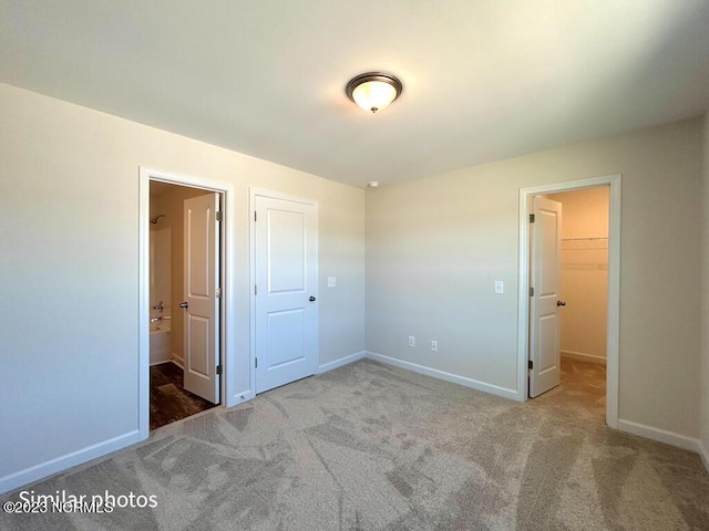 unfurnished bedroom with baseboards, ensuite bathroom, a walk in closet, carpet flooring, and a closet