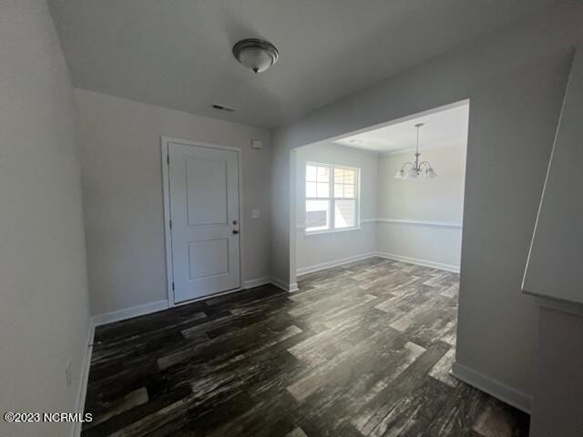 unfurnished dining area featuring a chandelier, visible vents, baseboards, and wood finished floors