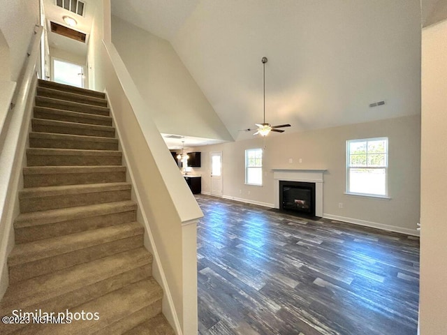 stairs featuring a fireplace with flush hearth, ceiling fan, wood finished floors, high vaulted ceiling, and baseboards