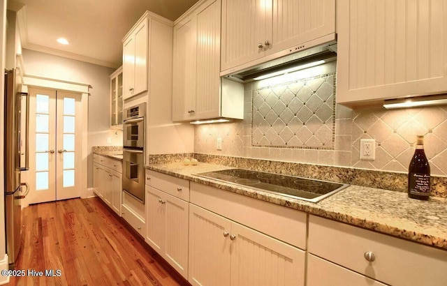 kitchen featuring appliances with stainless steel finishes, ornamental molding, wood finished floors, french doors, and under cabinet range hood