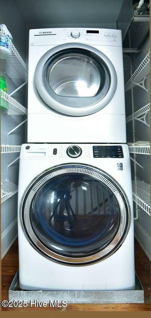 laundry area with stacked washer and dryer, wood finished floors, and laundry area