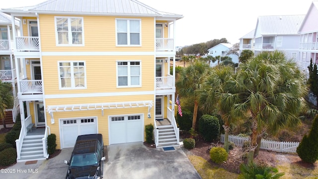 coastal home featuring concrete driveway, stairway, an attached garage, metal roof, and fence