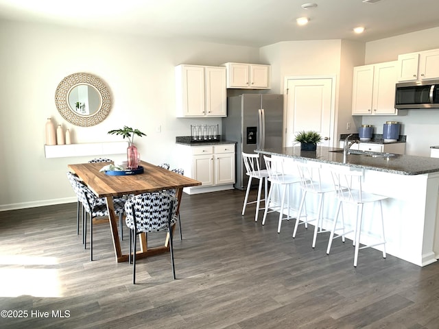 kitchen with dark stone counters, dark wood-style floors, a breakfast bar area, stainless steel appliances, and a sink