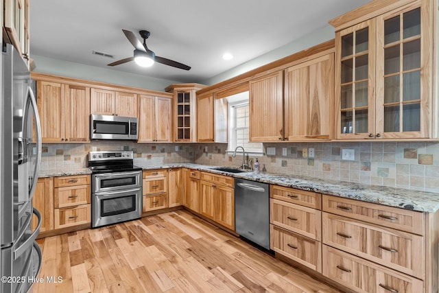 kitchen featuring light stone counters, light wood-style flooring, stainless steel appliances, a sink, and tasteful backsplash